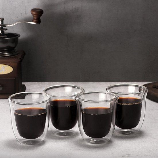 Quatre verres à double paroi avec liquide sombre, à côté d'un moulin à café.