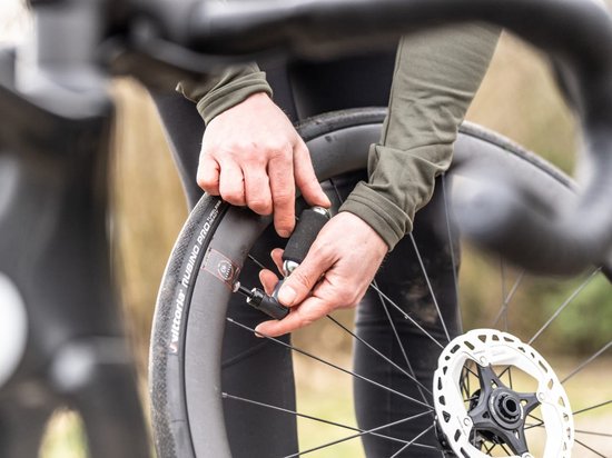 Handen gebruiken een zilveren CO2-patroon met zwarte hoes om een fietsband op te pompen.