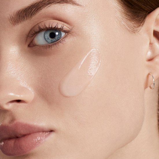 Close-up van een vrouwelijk gezicht met blauwe ogen, met een veeg hydraterend serum op de wang.