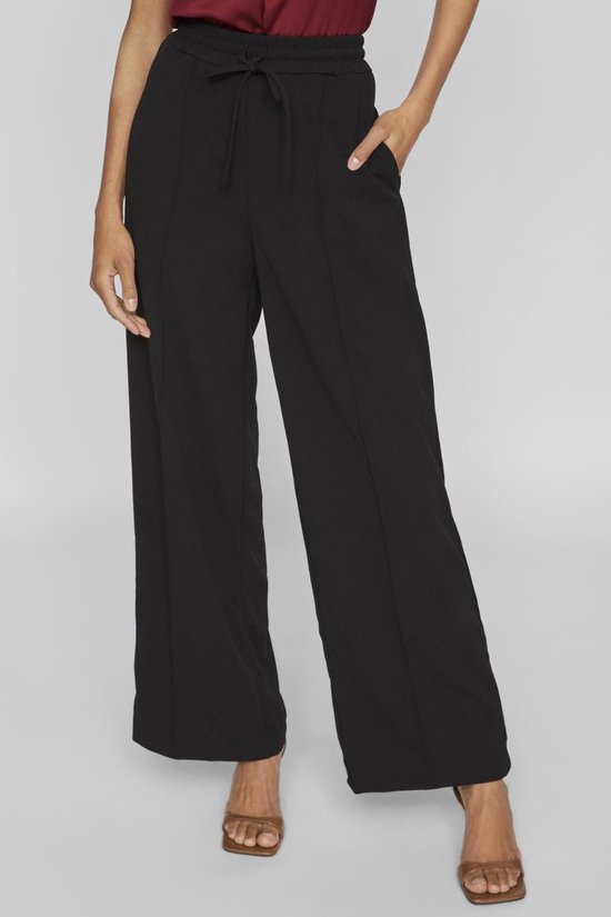 Zwarte wijde broek met trekkoord en steekzakken, gedragen met sandalen.