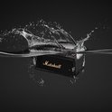 Zwarte Marshall-speaker met goudkleurig logo, half ondergedompeld in water met grote spatten.