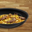 Zwarte koekenpan gevuld met gebakken biefstuk, aardappelen en uien, op een houten ondergrond.