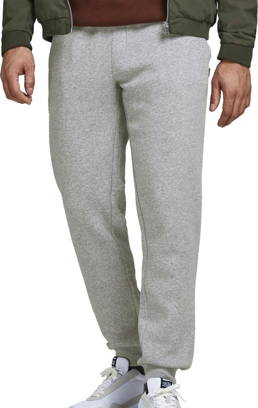 Lichtgrijze joggingbroek met witte sneakers, gedragen door een man met groene bomberjack.