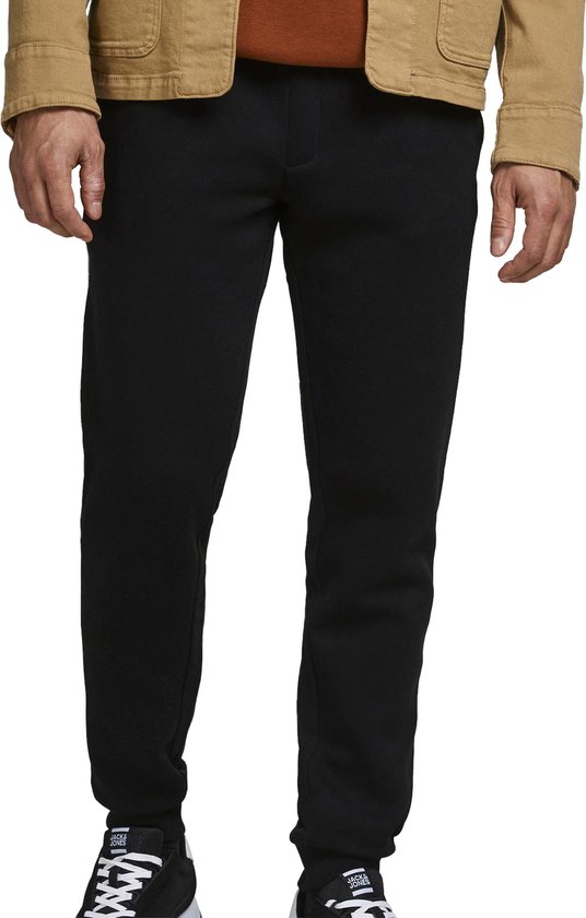 Man in een bruine jas met bruine hoodie en zwarte joggingbroek.