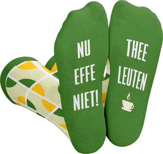 Groene sokken met witte tekst 'NU EFFE NIET!' en 'THEE LEUTEN' op de zolen, met een patroon van gele en groene halve cirkels op de zijkanten.