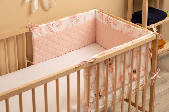 Babybed met bedbumper, beddengoed en matras. Bumper is wit met prinsessen en bloesems, en lichtroze gewatteerd.