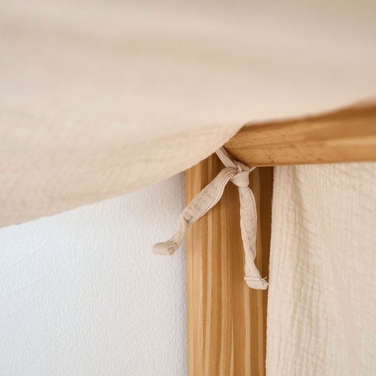 Ciel de lit en mousseline beige avec des rubans beiges attachés à un cadre de lit en bois.