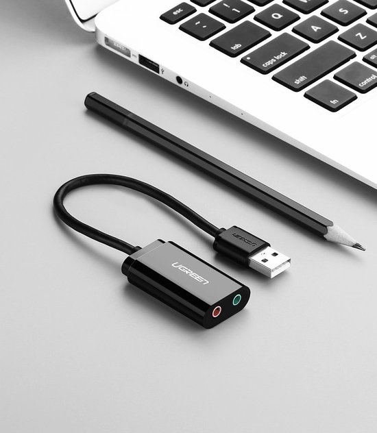 Zwarte UGREEN USB geluidskaart adapter naast een potlood op een bureau.