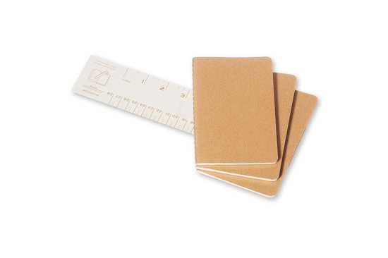 Drie bruine notitieboeken met een opengevouwen Moleskine notitieboek en een liniaal met inches en centimeters.