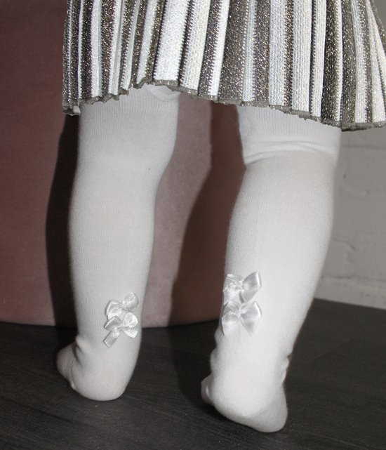 Witte maillot met satijnen strikjes onderaan de kuiten. Gekleed met een glinsterende rok.