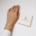 Pols met roségouden armband met hartvormig bedeltje met kristallen, naast geschenkdoos.