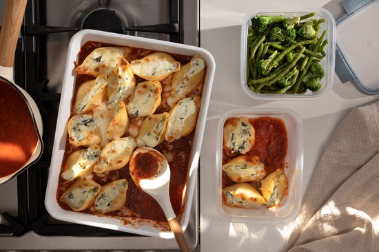 Plat allant au four avec des pâtes coquilles farcies dans une sauce tomate, à côté d'un plat de légumes.