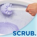 Een hand gebruikt een paarse toiletborstel om een toilet met schuimend water schoon te maken.