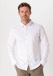 Man met kort bruin haar, draagt een wit overhemd met lange mouwen en een bruine broek, gezien van voren.