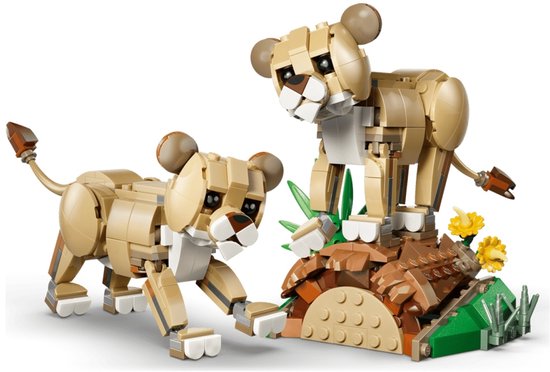 Twee LEGO leeuwenwelpen spelen met een stuk hout en groene bladeren op een bruine ondergrond met bloemen.
