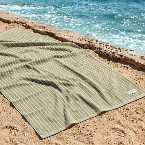 Groen gestreept strandlaken liggend op het zand bij de zee met een houten paaltje.