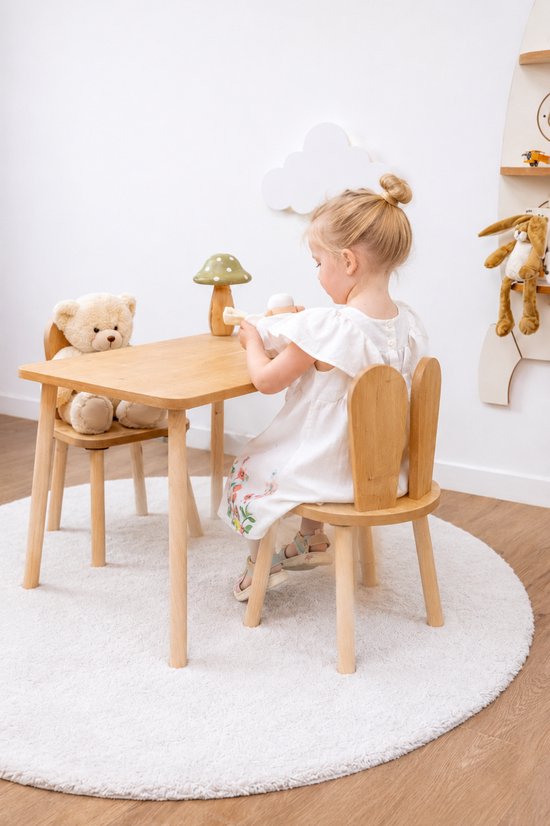 Houten kindertafel met twee stoeltjes met konijnenoren, een meisje speelt aan tafel.
