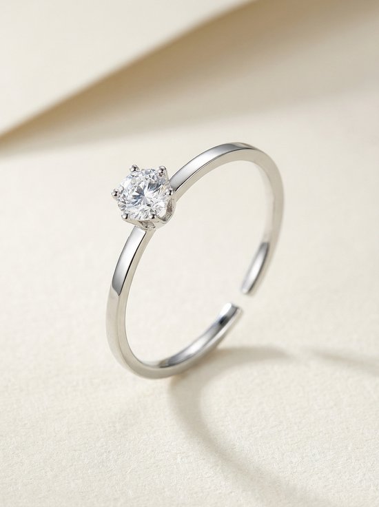 Bague argentée ajustable ornée d'une zircon, sur fond crème.