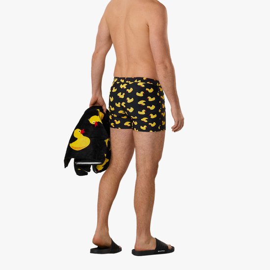 Man met rug naar kijker, zwembroek met badeendjesprint en zwarte handdoek met badeendjes