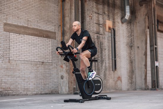 Man met zwart shirt en broek fietst op een zwarte Fit Bike Race Magnetic Pro spinfiets buiten.