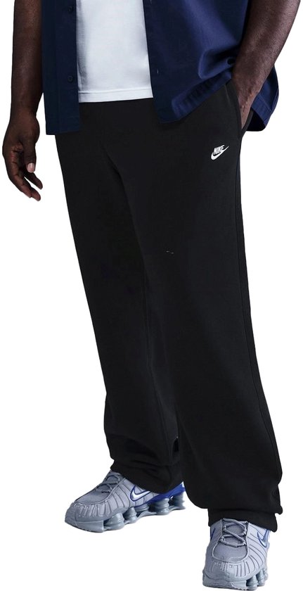 Man met de voorkant naar de camera, draagt een zwarte Nike trainingsbroek met klein Nike logo op de linkerheup.