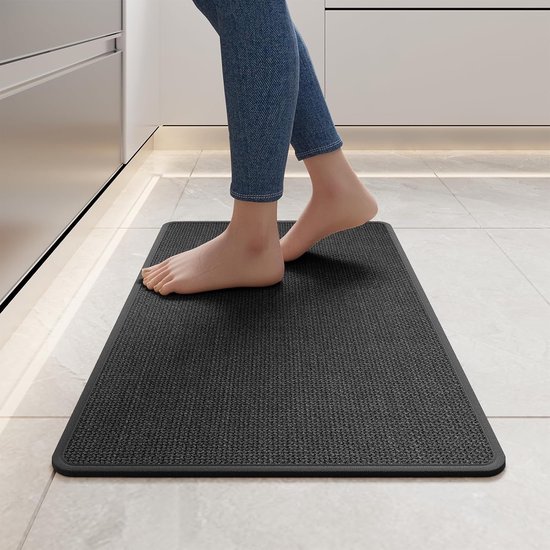 Pieds d'une personne sur un tapis de cuisine gris foncé avec un envers antidérapant.