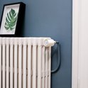 Netatmo slimme thermostaatknop, wit met oranje accent, op een crèmekleurige gietijzeren radiator.