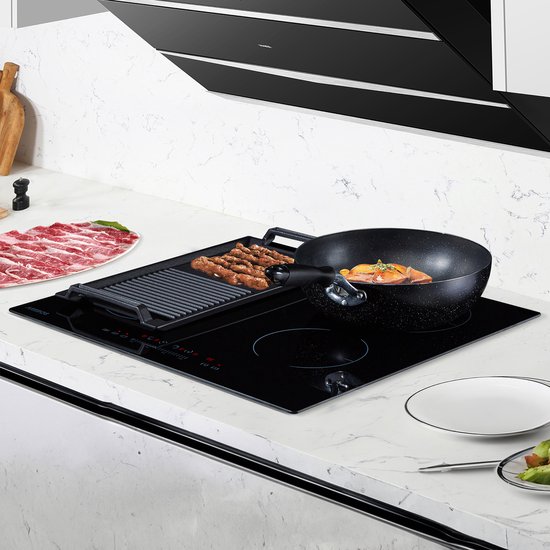 Zwarte grillplaat met worstjes en een wok met groenten op een zwarte inductiekookplaat.