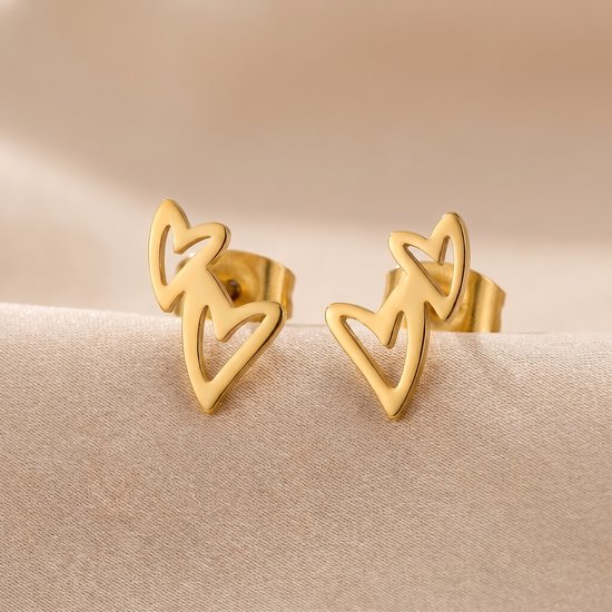 Clous d'oreilles dorés en forme de cœur sur tissu crème.