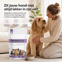 Vrouw die een goudkleurige doodle hond aait naast een verpakking 'Probiotica + Prebiotica voor Honden'.