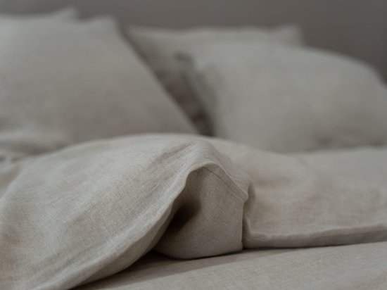Gedrapeerde beige linnen dekbedovertrek en kussens met zachte plooien.