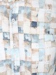 Detail van de knopenrij van een langarmig overhemd met een mozaïekprint van blauwe, beige en witte vierkanten.