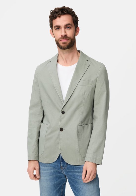 Man met baard draagt een lichtgroen Camel Active colbert met bruine knopen, wit T-shirt en jeans.