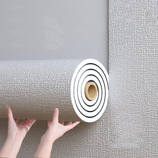 Un rouleau de papier peint texturé gris clair tenu par des mains lors de l'application sur un mur.