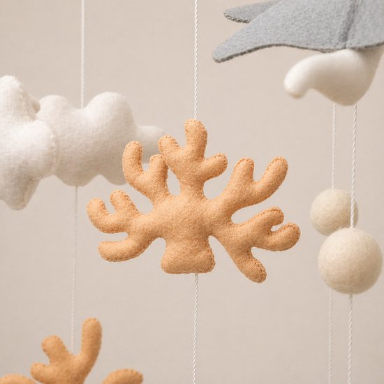 Zachte, beige vilten koraalfiguur hangt aan een draad met wolken.