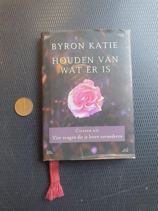 Boek 'Houden van wat er is' van Byron Katie met roze roos en roze leeslint. Naast een muntstuk.