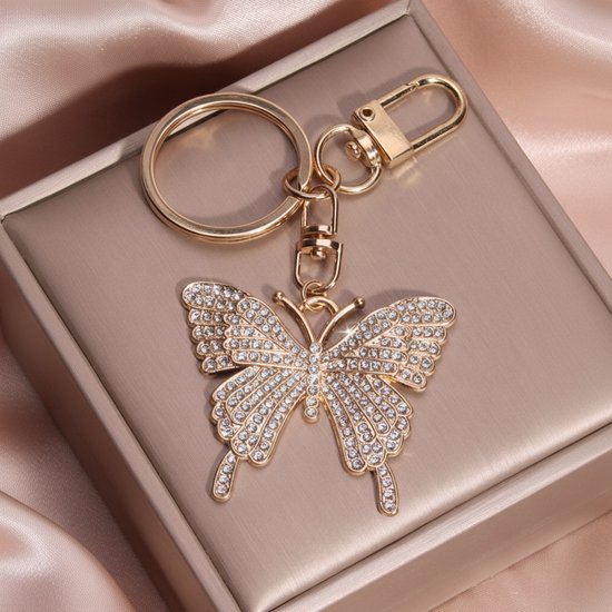 Gouden sleutelhanger met vlinderhanger bezet met strass, op een beige doos.