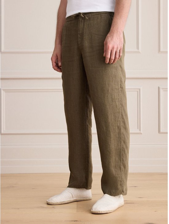Zijaanzicht van de olijfgroene linnen broek met relaxte pasvorm op model.