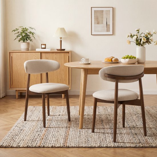 Twee beige gestoffeerde eetkamerstoelen met houten frame, naast een houten eettafel.