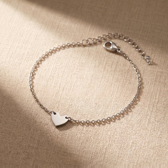 Zilverkleurige schakelarmband met een klein hartje aan een beige ondergrond.