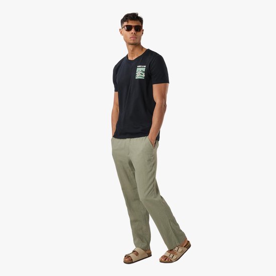 Man met zonnebril en zwarte t-shirt met schildpaddenprint, gekleed in groene broek en sandalen.
