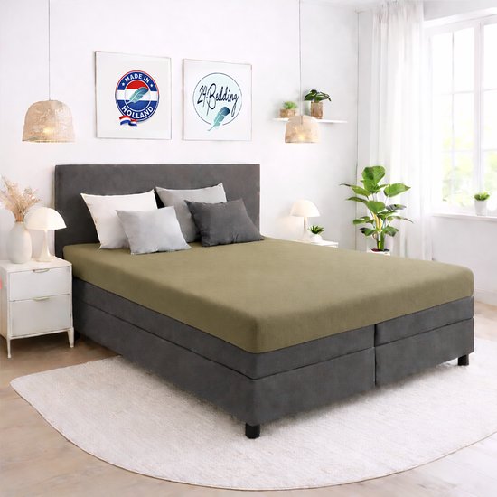 Een tweepersoonsbed met een olijfgroen hoeslaken. De nachtkastjes zijn wit met gouden knoppen.