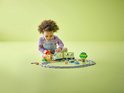Un jeune enfant joue joyeusement avec un train vert clair, des rails, une petite maison et un arbre.