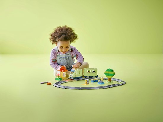 Un jeune enfant joue joyeusement avec un train vert clair, des rails, une petite maison et un arbre.