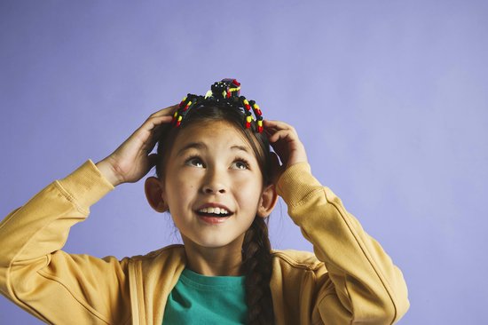 Een jong meisje met een vlecht kijkt omhoog met een LEGO spin op haar hoofd.