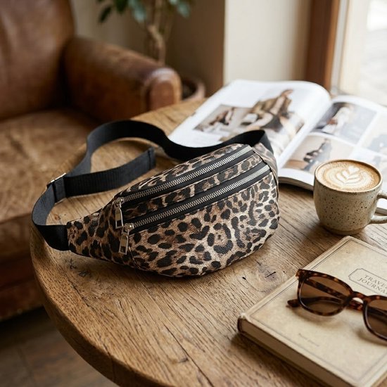 Heuptas met luipaardprint op een houten tafel met koffie en tijdschrift.