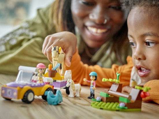 Mère et enfant jouant avec des jouets de cheval LEGO Friends, y compris une voiture, une remorque et des chevaux.