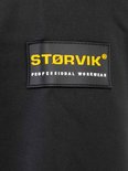Zwart label met geel "STØRVIK PROFESSIONAL WORKWEAR" logo op een zwarte jas.