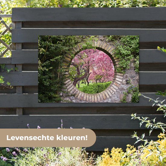 Une affiche de jardin avec une ouverture circulaire en pierre révélant des arbres roses en fleurs, accrochée à une clôture.