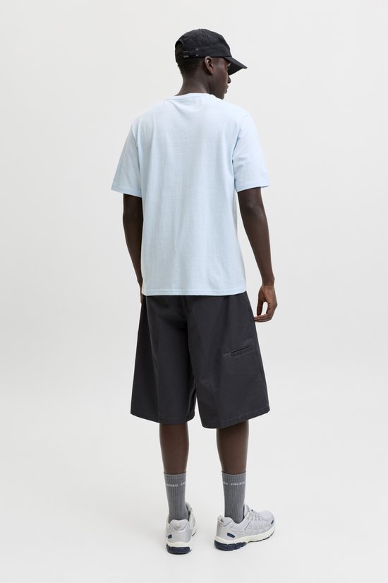 Man met donkere huid in lichtblauwe t-shirt, grijze korte broek en zwarte pet, achterkant.